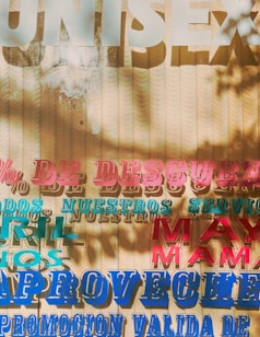 A textured background with layered, colorful text in various fonts and sizes. The words are written in Spanish, mentioning discounts and promotions. Shadows of leaves create an artistic overlay on the surface.