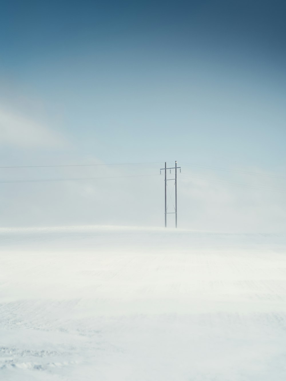 palo elettrico nero su terreno coperto di neve sotto cielo blu durante il giorno
