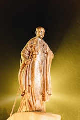 A serene statue of Saint Jude Thaddaeus holding a staff, bathed in soft golden light.