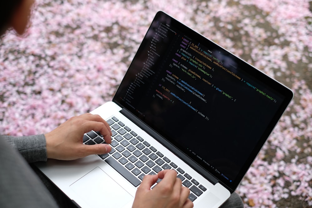 person using macbook pro on pink and white floral textile