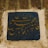 Arabic calligraphy with elegantly curved letters on a deep blue ceramic tile, set into a weathered stone wall.