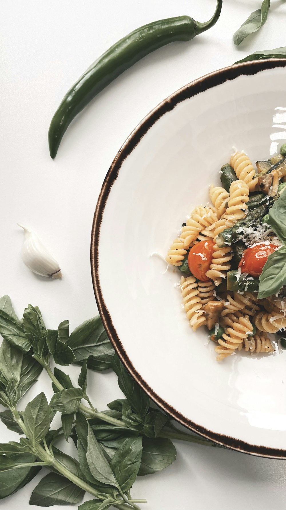 Nudeln mit geschnittenen Tomaten und grünem Blatt auf weißem Keramikteller