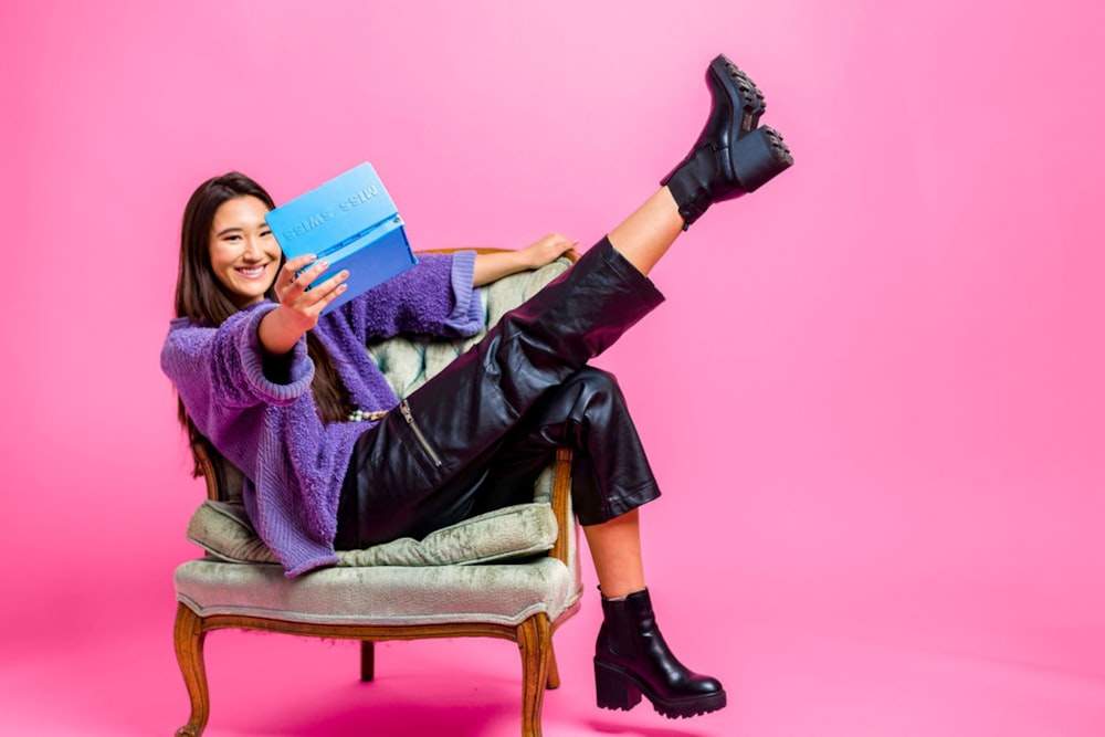 woman in purple long sleeve shirt sitting on brown wooden armchair reading book