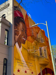 A candid moment of a smiling artist painting a mural on a bright city wall.