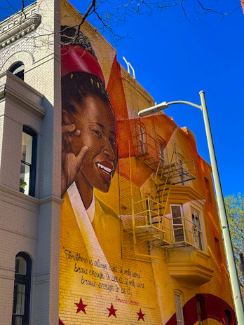 A candid moment of a smiling artist painting a mural on a bright city wall.