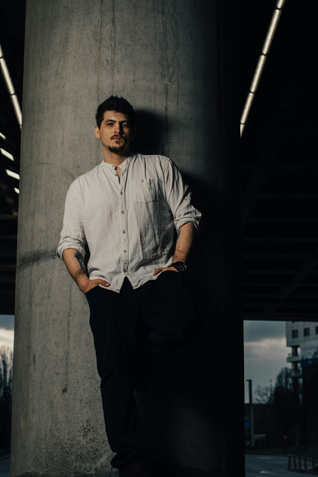 man in white button up shirt and black pants standing beside gray concrete wall during daytime