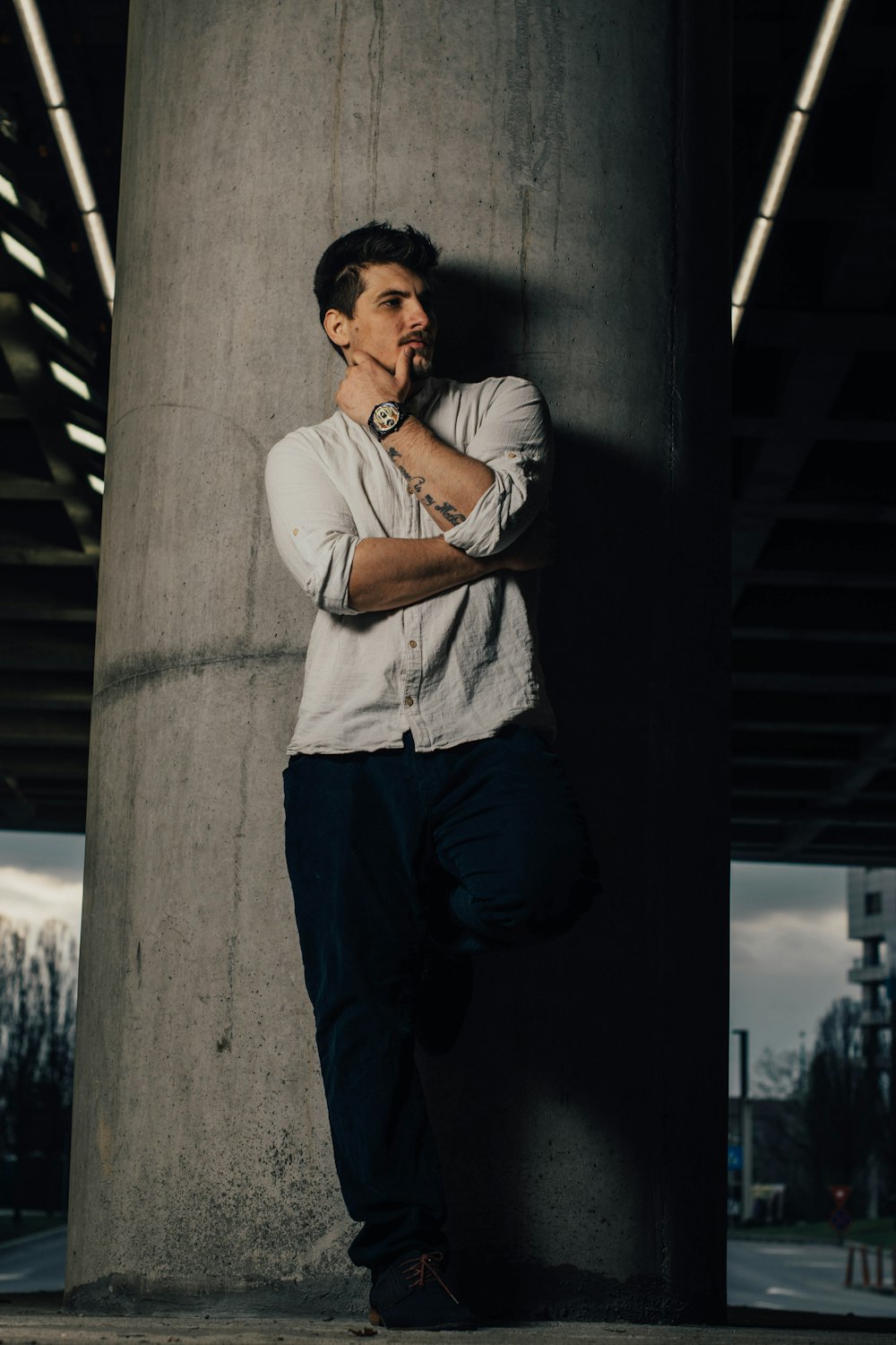 hombre con camiseta blanca y pantalones negros apoyados en la pared