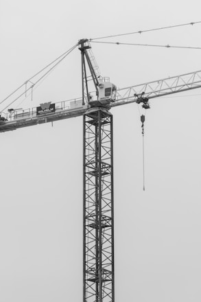 A rugged crane lifting steel beams on a busy construction site under a gray sky.