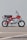 A vintage red motorcycle with a black seat and chrome accents is parked on a concrete surface against a plain gray backdrop. The motorcycle features a prominent Honda logo on the side, along with knobby tires designed for off-road use.