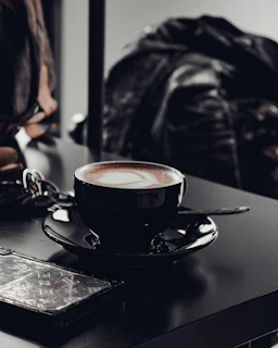 A sleek wallet with a gingko leaf embossed, placed next to a cup of coffee on a café table.