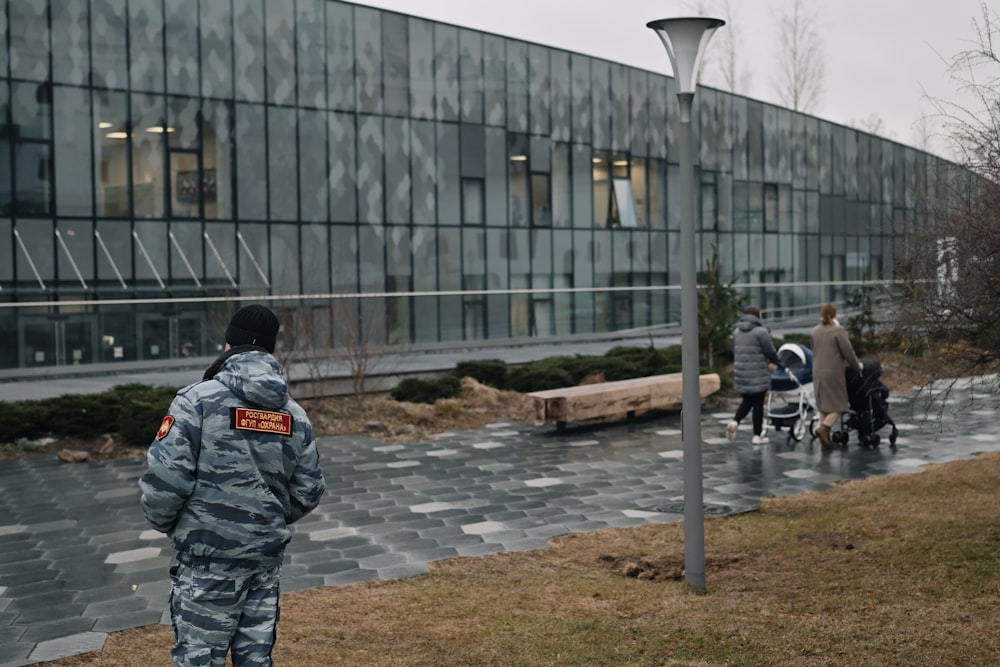 man in black and green camouflage jacket standing near gray concrete building during daytime