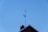 A TV antenna is mounted on the roof of a building with a clear blue sky in the background. The roof features a chimney and has a triangular peak.