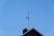 A TV antenna is mounted on the roof of a building with a clear blue sky in the background. The roof features a chimney and has a triangular peak.