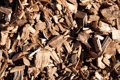 A close-up view of a pile of wood chips in various shades of brown. The wood pieces are irregularly shaped and vary in size, showing rough textures and fibrous details.