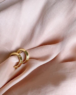 Close-up of delicate wedding rings resting on a soft pink powder fabric background.
