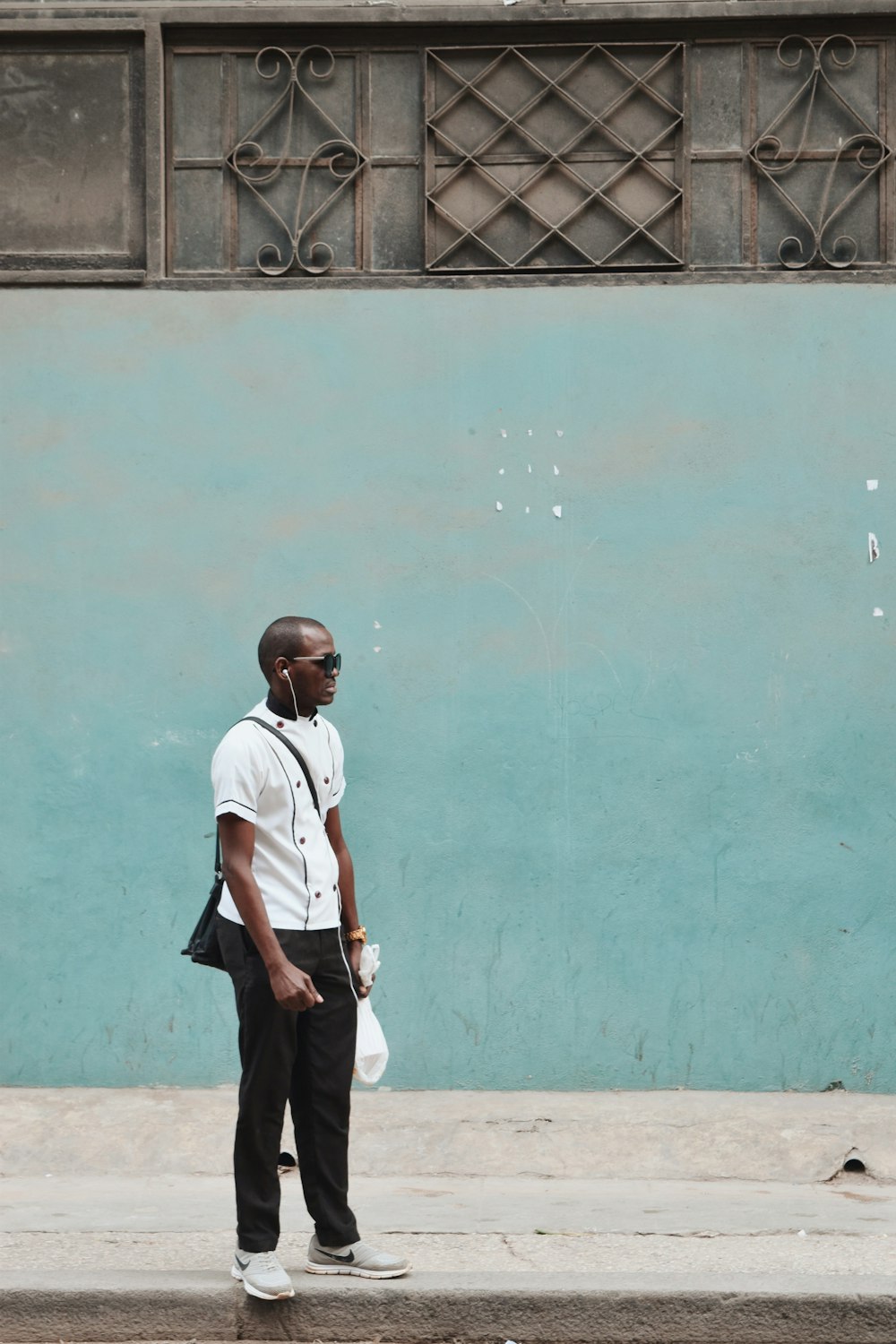 man in white polo shirt and black pants standing beside green wall