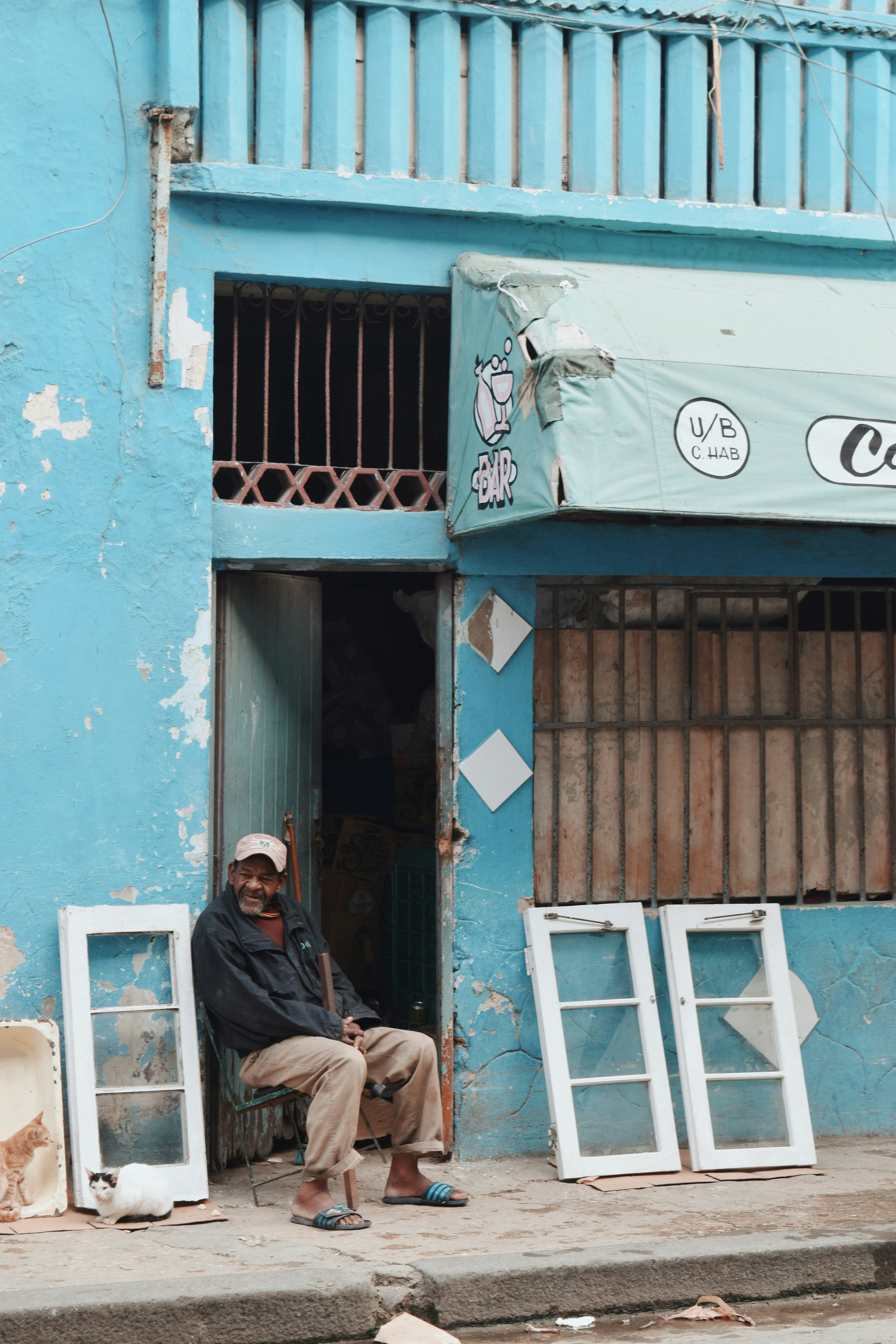 Man sitting in front of a Cuban building with two cats