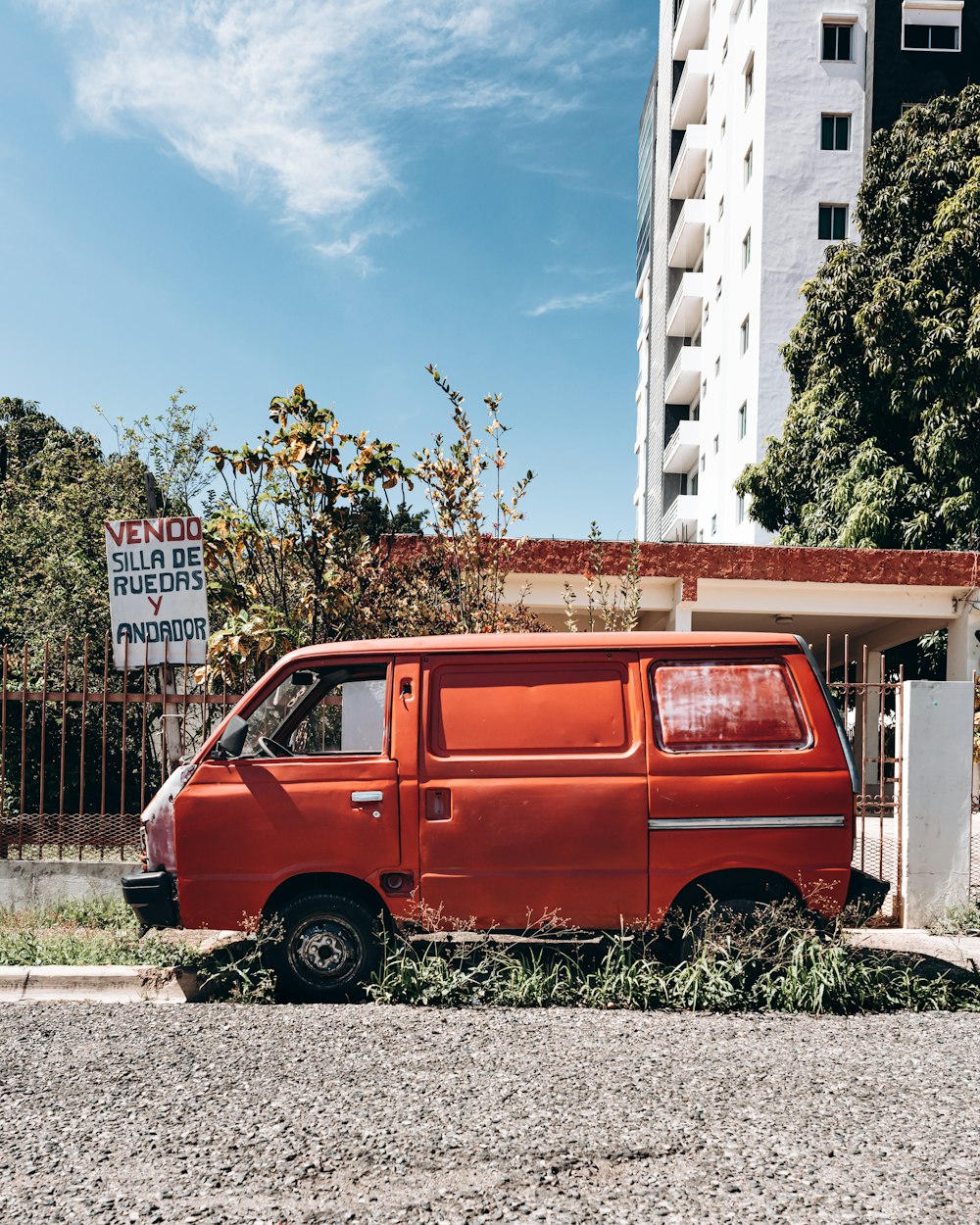 Furgoneta roja estacionada junto a un edificio blanco y marrón durante el día