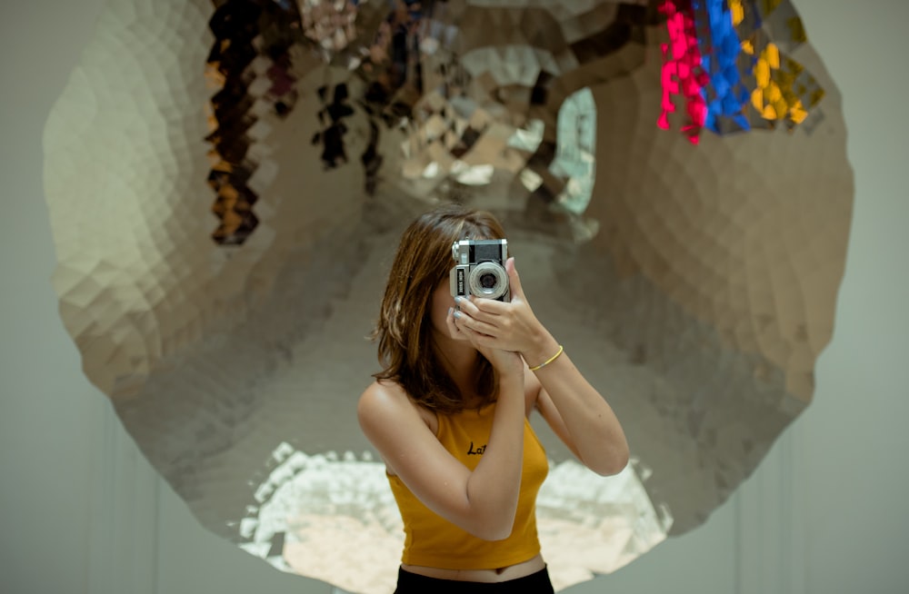 woman in yellow tank top holding silver and black camera