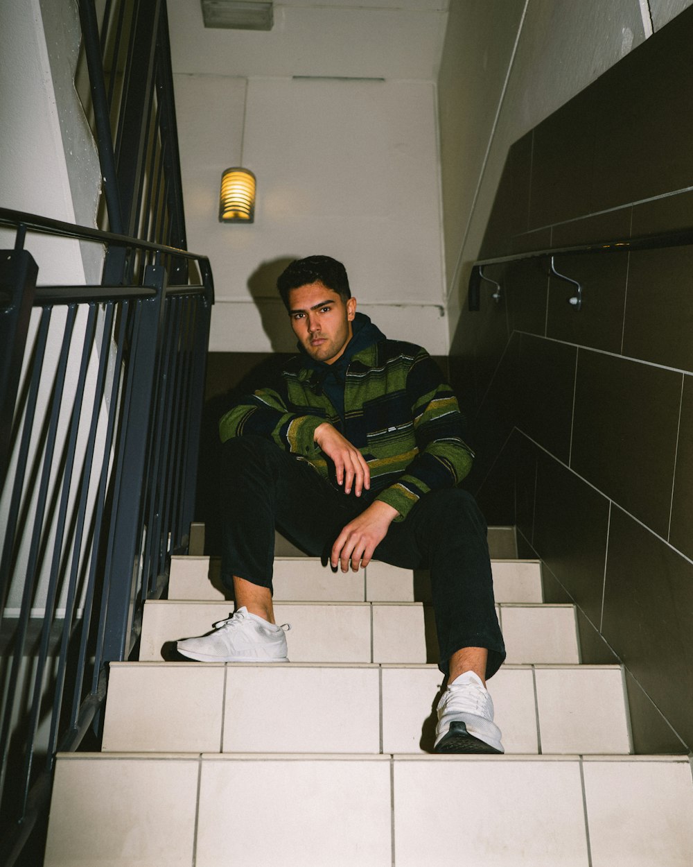 man in green and black jacket sitting on white ceramic floor tiles