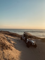 A serene view of the Emerald Sea with a 4x4 parked on the sandy shore at sunset.