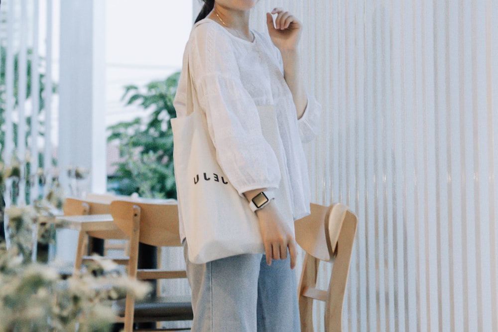 woman in white long sleeve shirt and blue denim jeans standing near brown wooden chair during