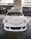 A customized white car is parked in a garage with a prominent front bumper and grill design. The windshield displays text decals reading 'THIS SHIT BUSSIN' and 'Royal Spades'. The background includes concrete pillars and a chain-link fence.