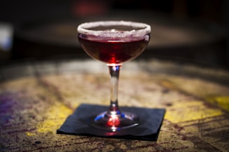 Close-up of a classic coupe glass filled with a deep red cocktail, resting on a polished wooden bar.