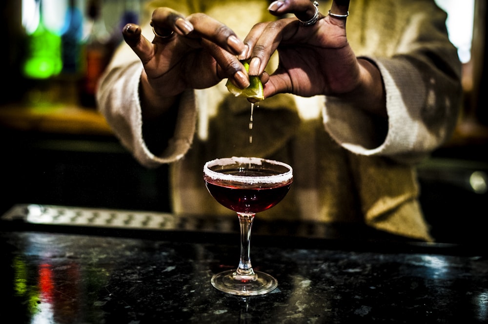 person holding clear wine glass with red wine