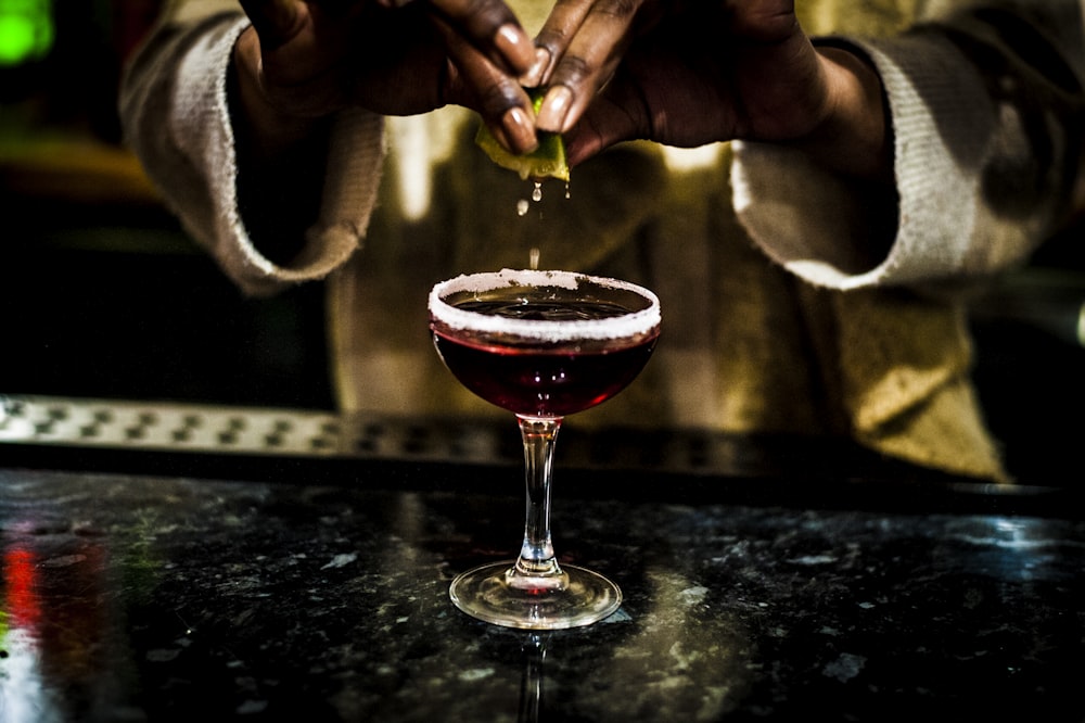 person holding clear wine glass with red liquid