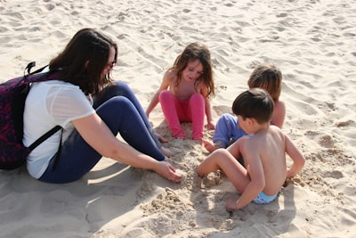 Kids playing in the sand with their mom at the beach.