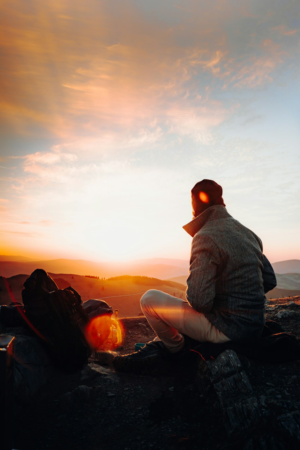 Mann in grauer Jacke sitzt bei Sonnenuntergang auf Felsen