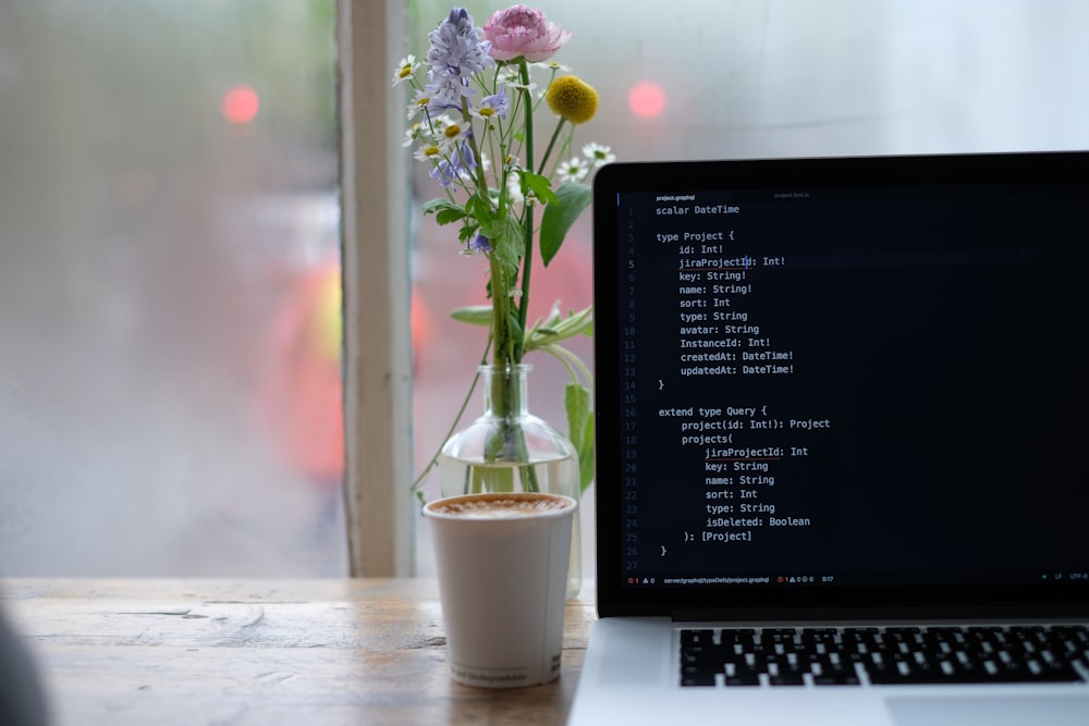 purple flowers in white ceramic vase beside black laptop computer