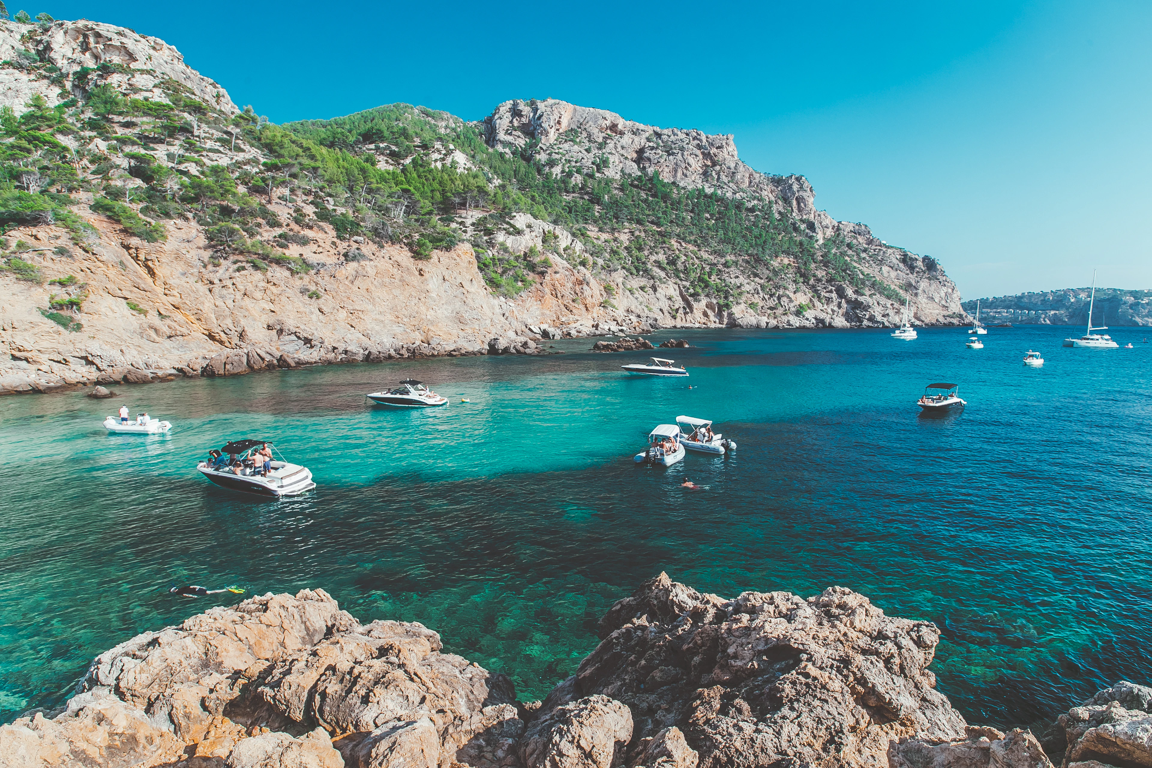 Boats moored in a turquoise rocky cove beneath limestone cliffs in Mallorca