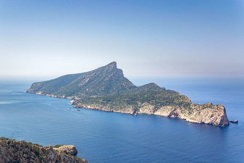 montagne verte et brune à côté de la mer bleue sous le ciel bleu pendant la journée