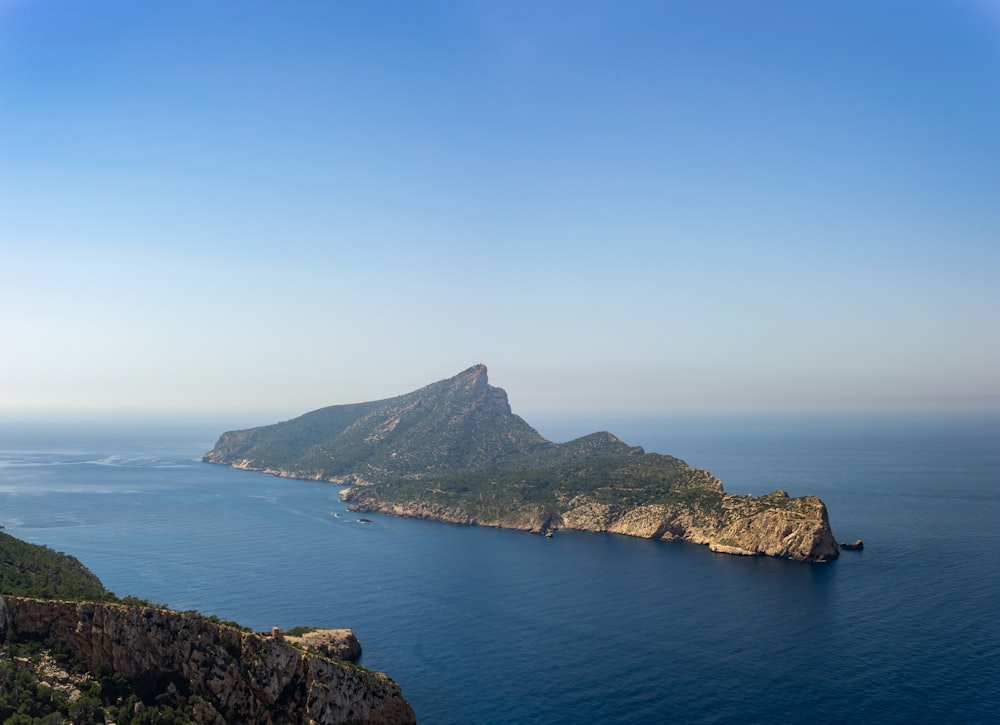 green and brown mountain beside blue sea under blue sky during daytime