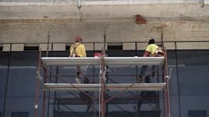 man in yellow jacket standing on red metal ladder