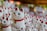 A collection of ceramic cat figurines featuring white bodies, red ears, and collars. The cats have one paw raised as if waving and are adorned with green eyes and small golden bells hanging from their necks.
