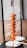 A skewer holds several pieces of marinated paneer interspersed with slices of onions and tomatoes. The ingredients are coated in a rich, spicy orange marinade. The skewer is held vertically, and there are blurred kitchen containers in the background.