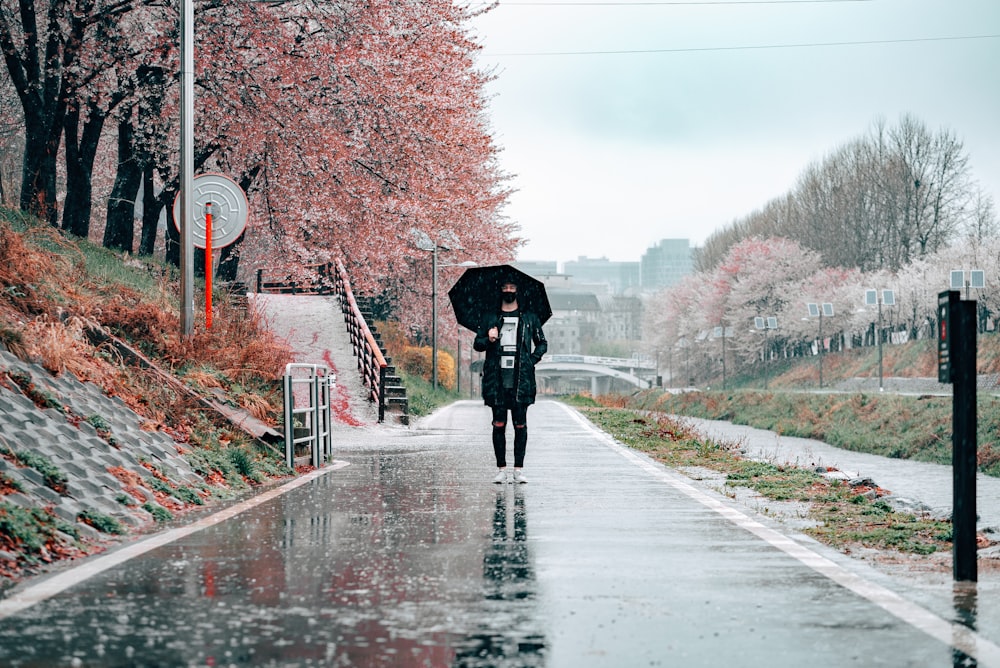 persona in cappotto nero che tiene l'ombrello che cammina sulla strada durante il giorno