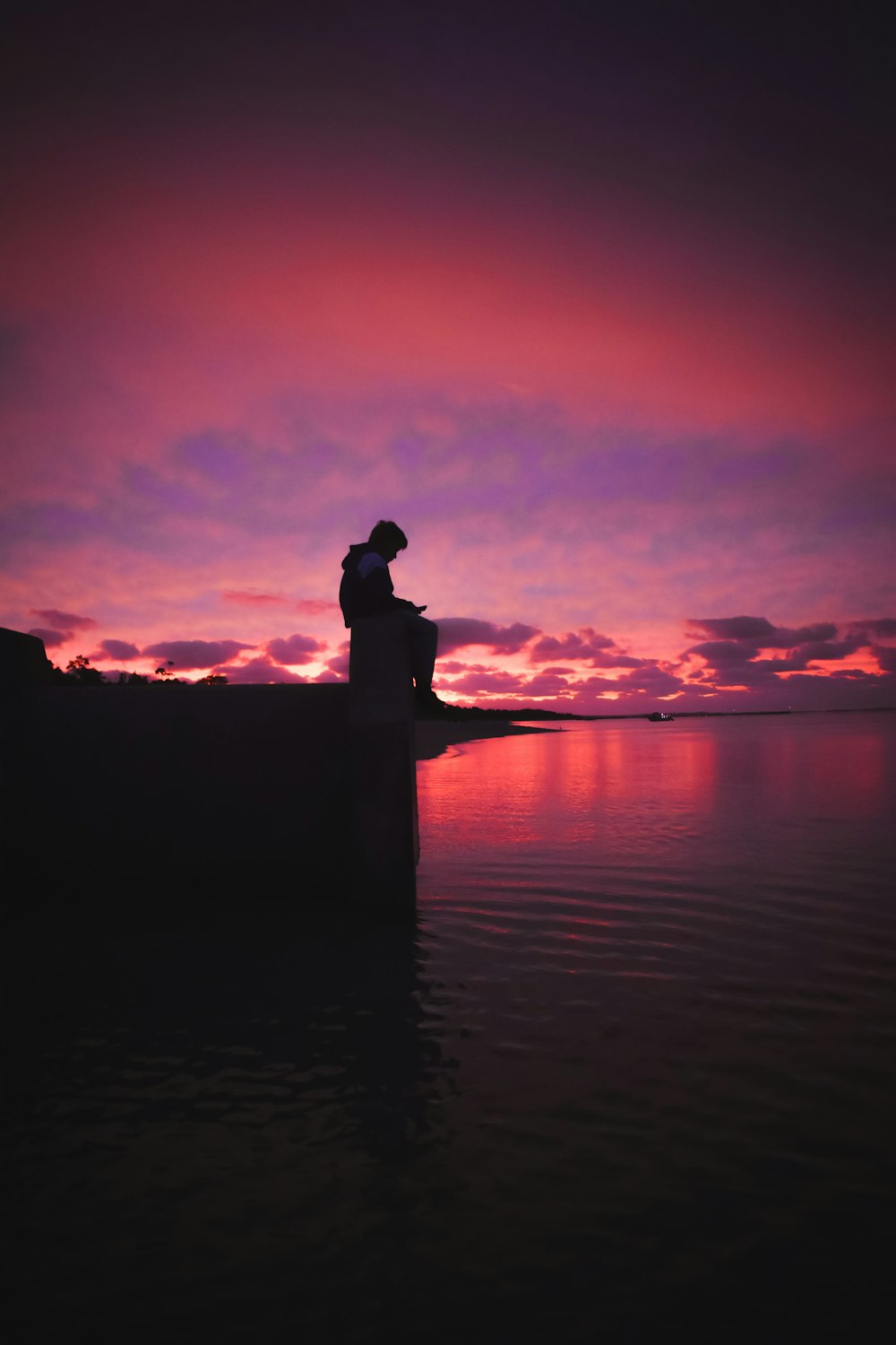 silhouette of man standing on rock formation near body of water during sunset