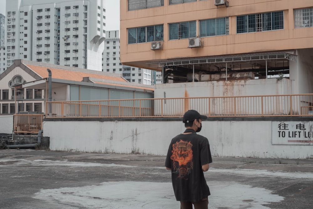 man in black and orange jacket standing near building during daytime