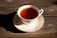 Close-up of a rustic handcrafted porcelain tea cup filled with steaming tea on a wooden table.