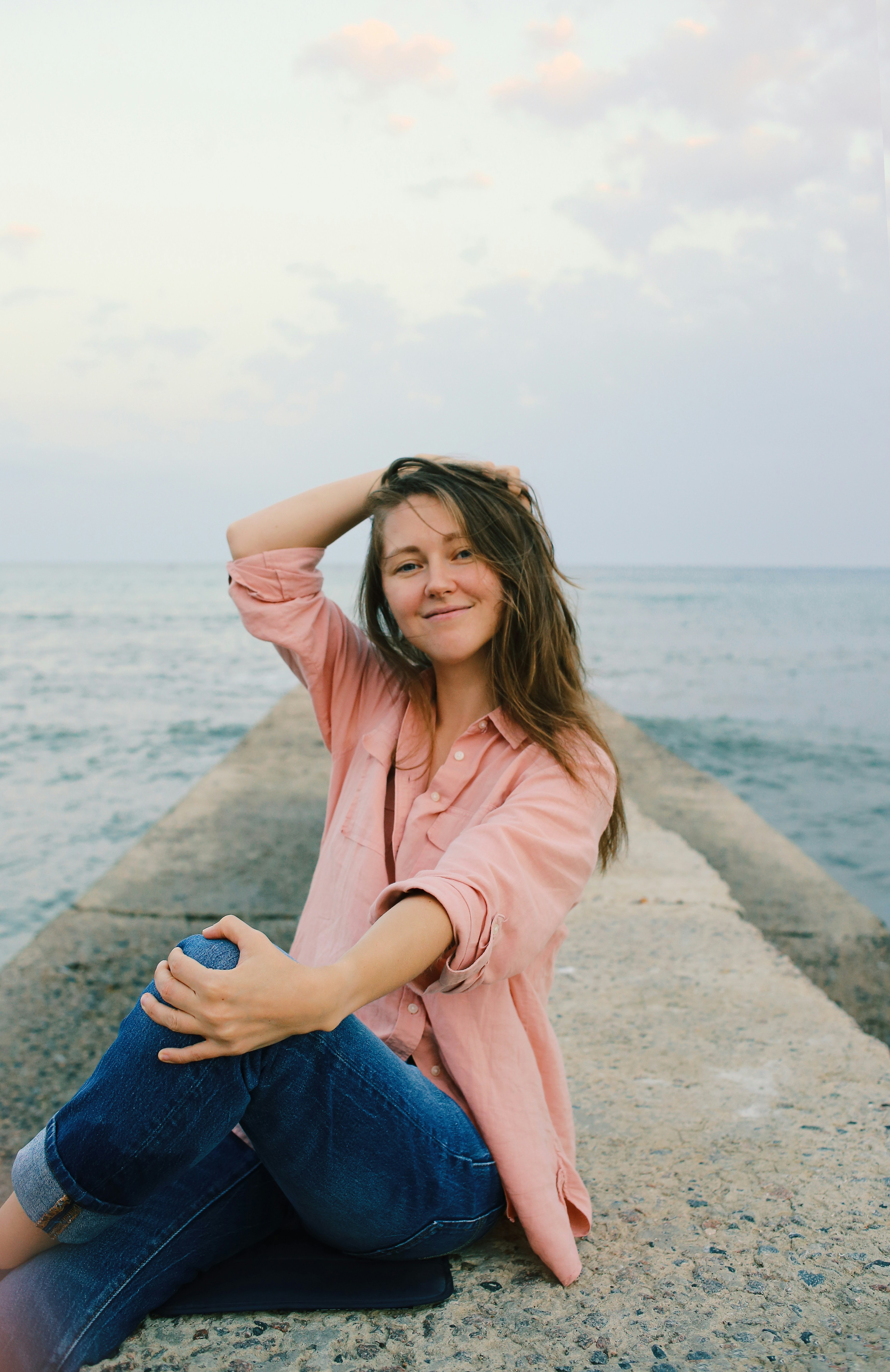 Woman in pink button up shirt and blue denim jeans sitting on gray