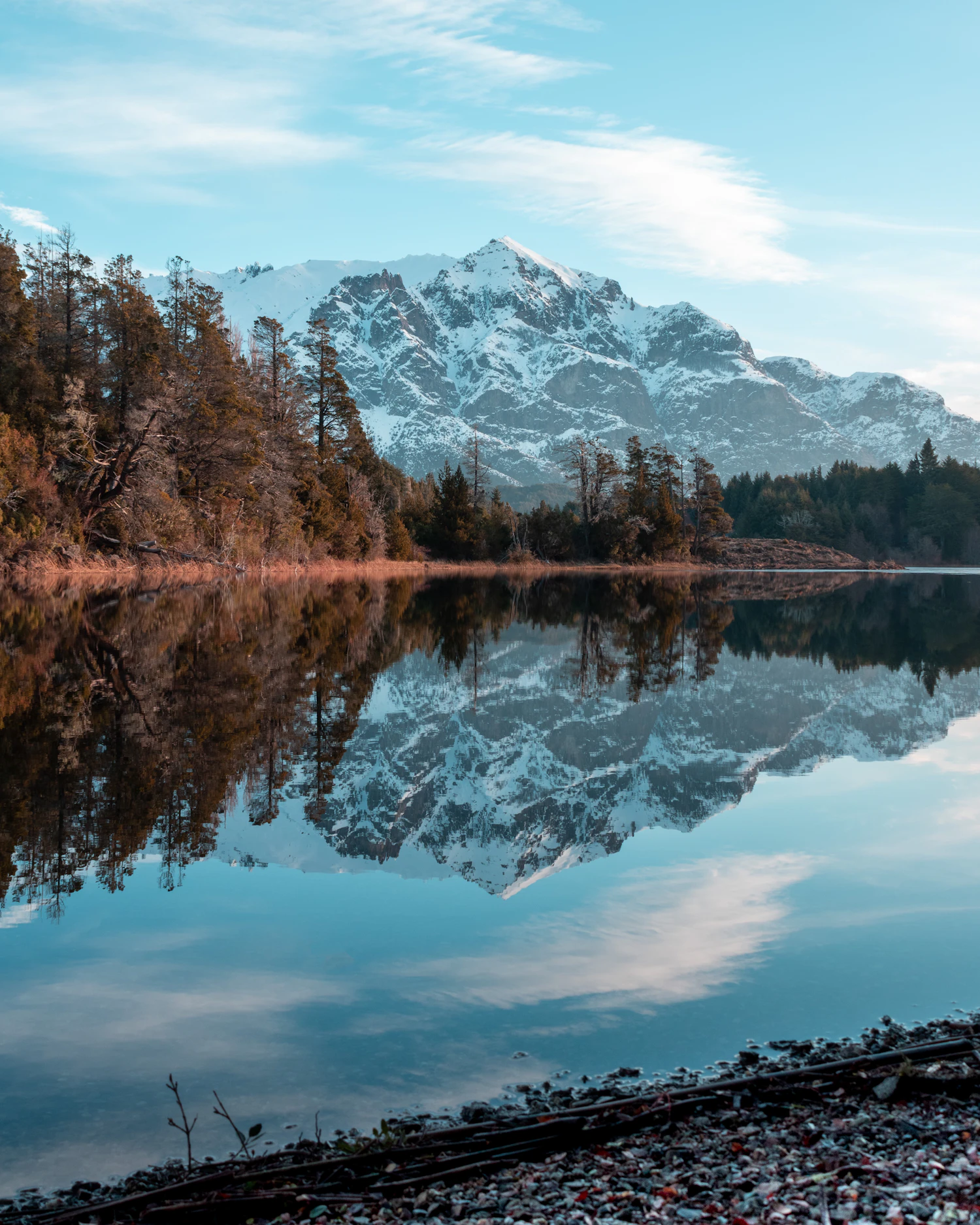 Autumn-tinged shoreline trees reflected in calm water under a rocky peak