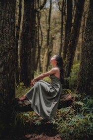 woman in black dress sitting on ground surrounded by trees