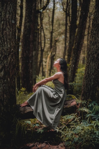 woman in black dress sitting on ground surrounded by trees