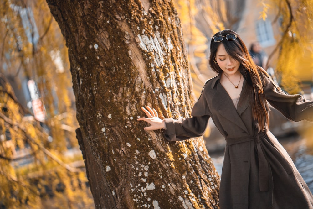 woman in black coat standing beside brown tree during daytime