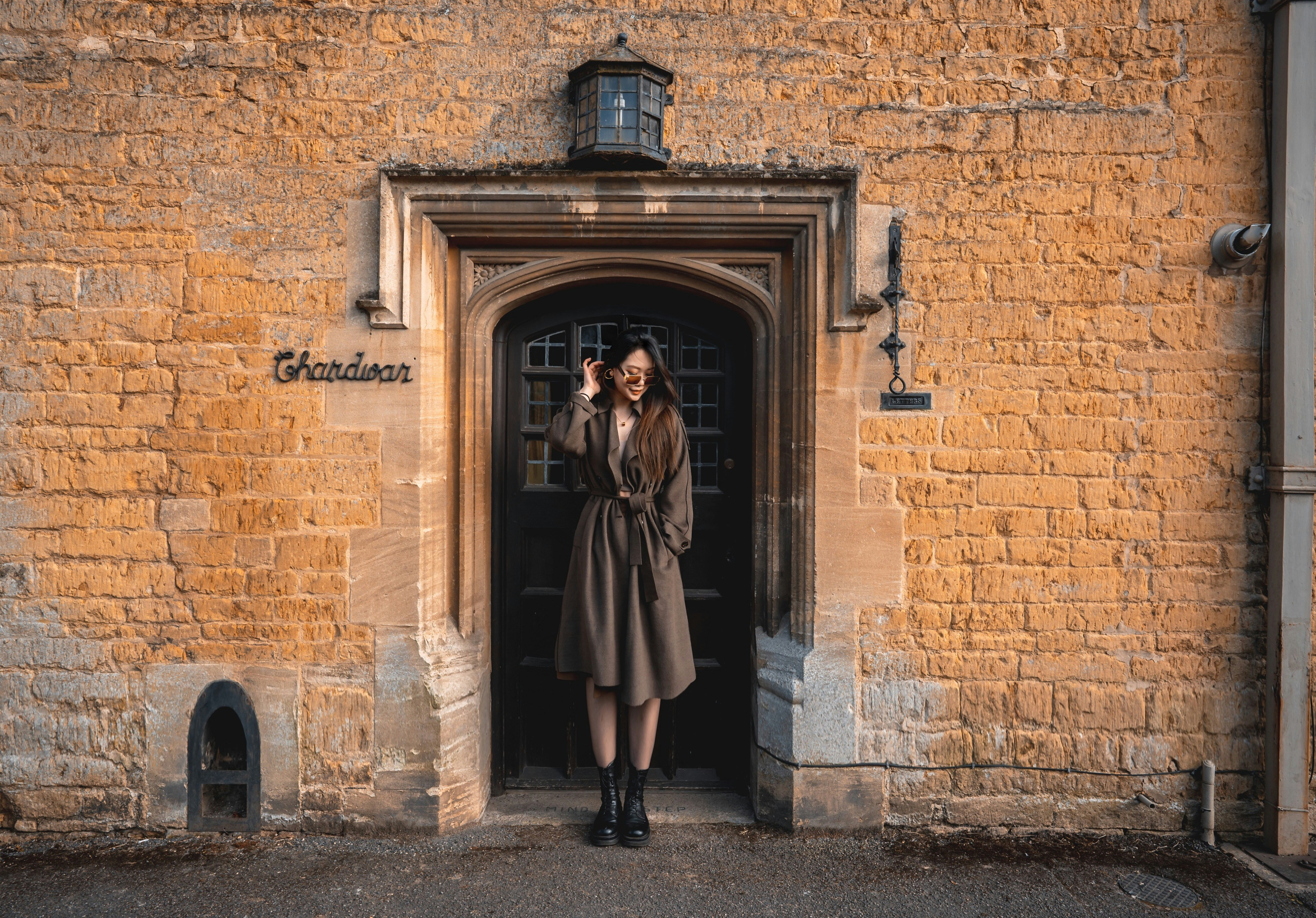 woman in brown coat standing in front of brown brick wall