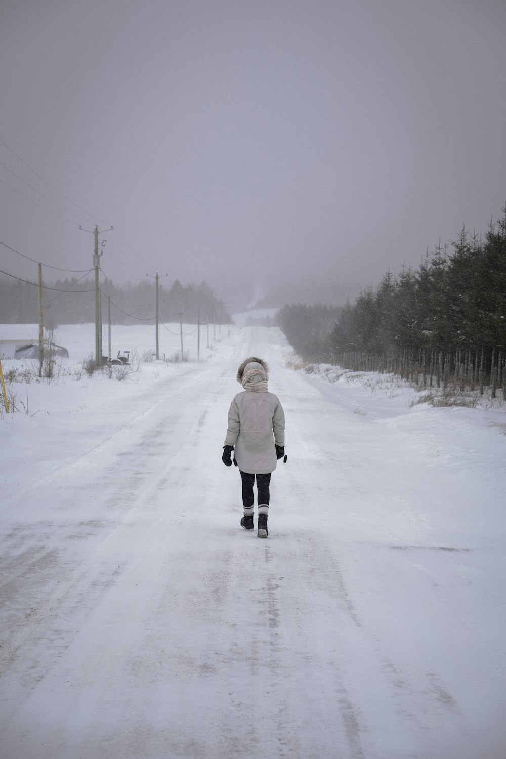 person in white coat walking on snow covered road during daytime